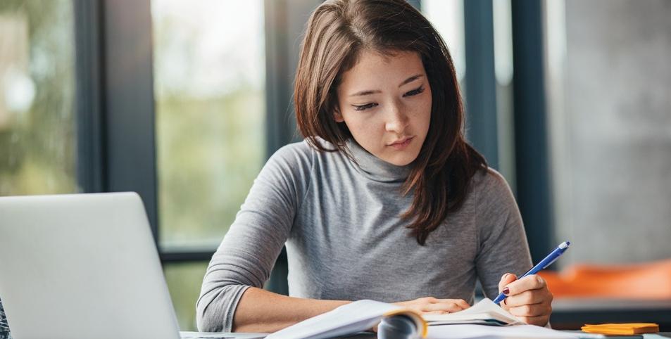 Shot of young woman taking down notes in diary. Female university student preparing note for the exam at library.